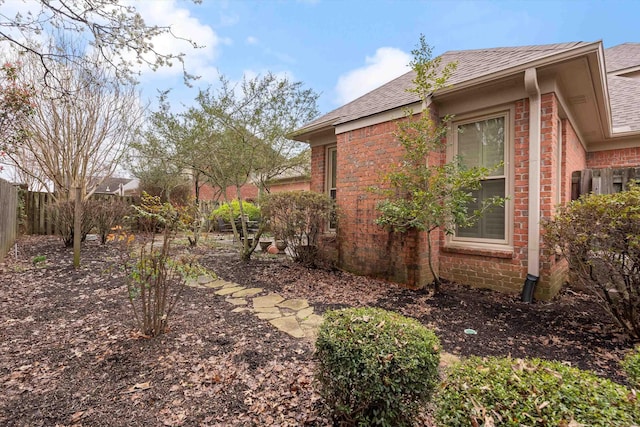 view of property exterior with brick siding, roof with shingles, and fence