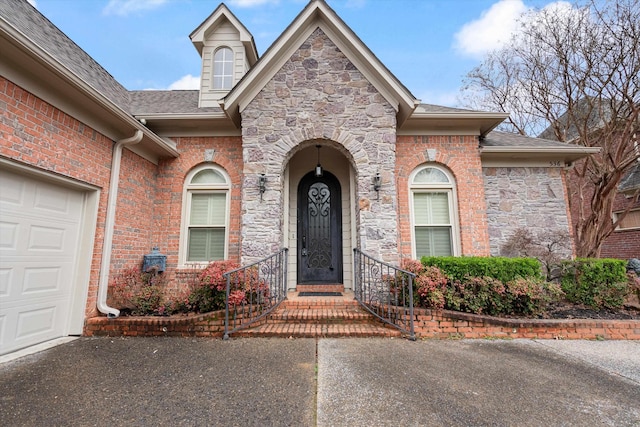 view of exterior entry featuring brick siding, stone siding, a shingled roof, and a garage