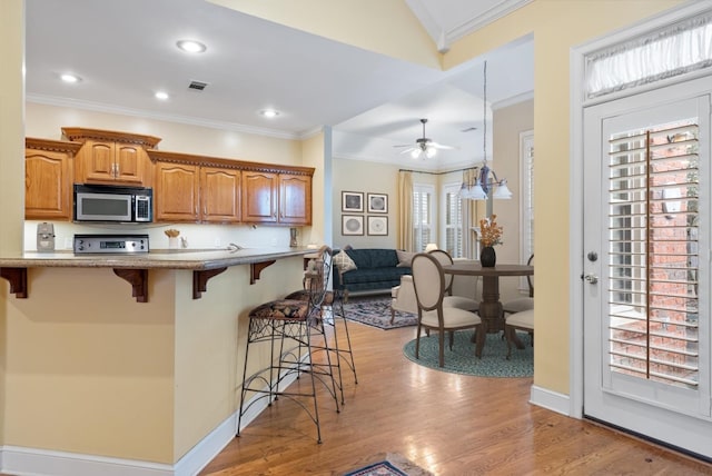 kitchen with stainless steel microwave, a breakfast bar, ornamental molding, light wood-style flooring, and range