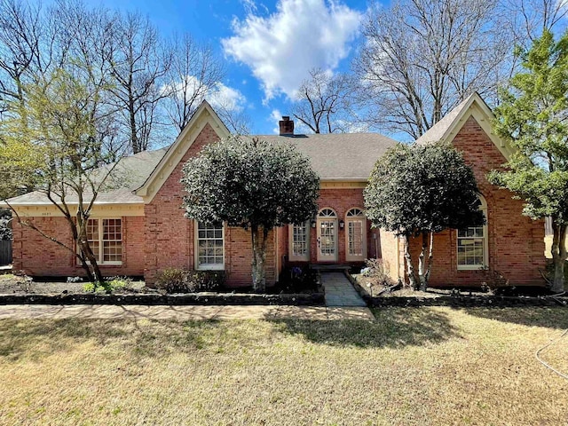 ranch-style house featuring brick siding, a chimney, a front yard, and roof with shingles