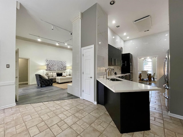 kitchen with a peninsula, a sink, light countertops, a towering ceiling, and open floor plan