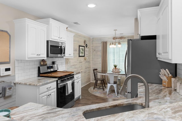 kitchen with light stone countertops, appliances with stainless steel finishes, wood finished floors, white cabinetry, and a sink