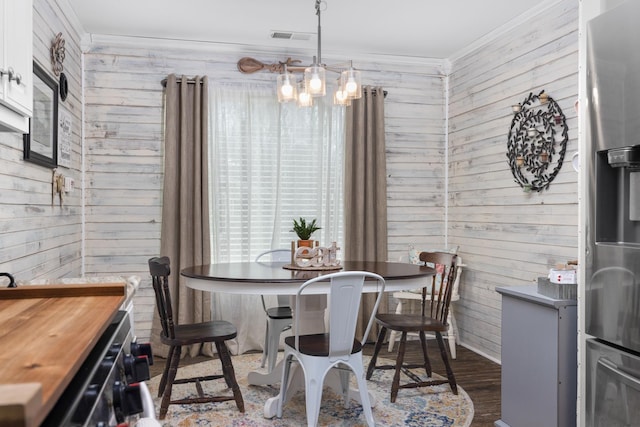 dining area with crown molding, wooden walls, visible vents, and a chandelier