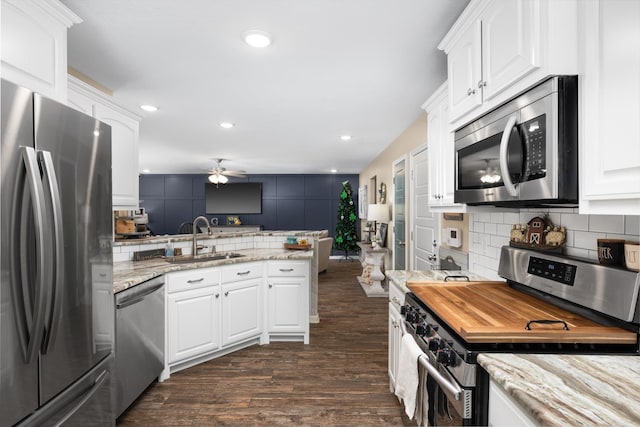 kitchen with dark wood-style floors, a peninsula, a sink, stainless steel appliances, and backsplash