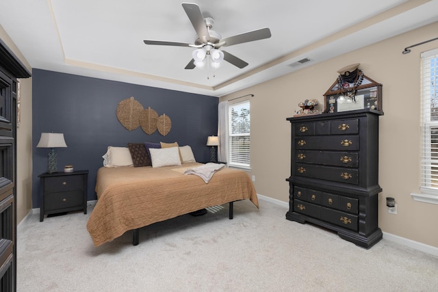 bedroom featuring light colored carpet, baseboards, and a tray ceiling