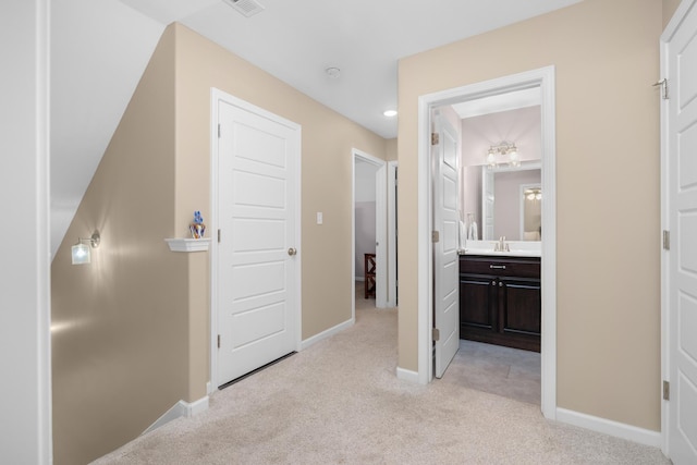 corridor with light colored carpet, baseboards, and a sink