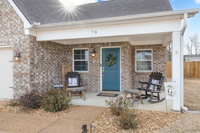 view of exterior entry featuring brick siding, a shingled roof, fence, a porch, and a garage