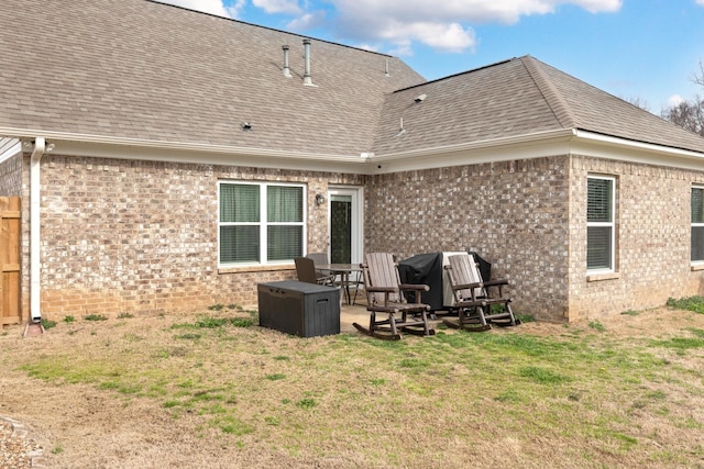 back of property with a patio, brick siding, roof with shingles, and a lawn