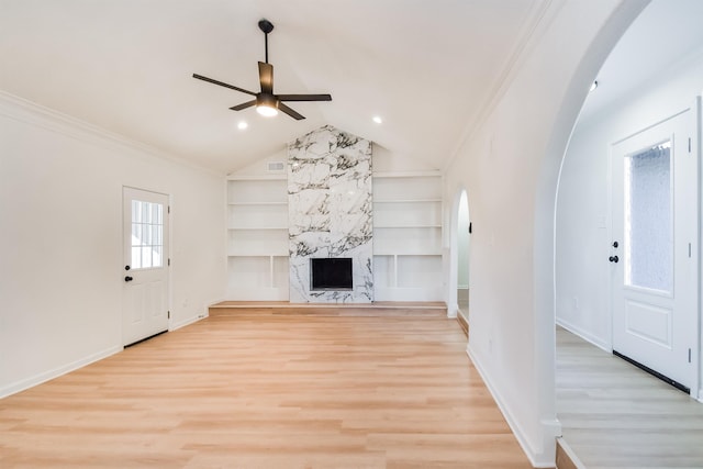 unfurnished living room featuring built in shelves, light wood-style flooring, ornamental molding, arched walkways, and a fireplace