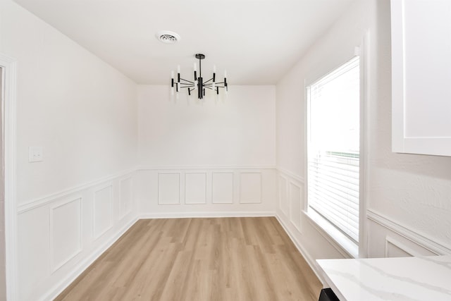 unfurnished dining area with a wainscoted wall, visible vents, a chandelier, and light wood-type flooring