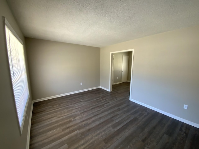 unfurnished room with dark wood-style floors, a textured ceiling, and baseboards