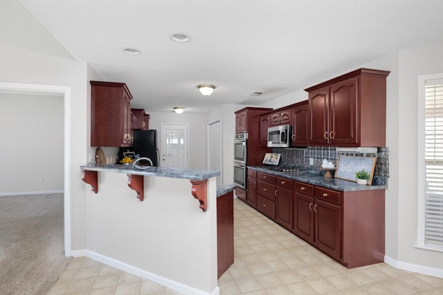 kitchen with tasteful backsplash, dark brown cabinets, a kitchen bar, a peninsula, and stainless steel appliances