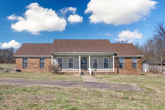 view of front of home featuring brick siding, covered porch, a front yard, and roof with shingles