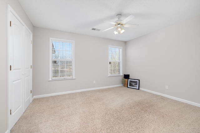 carpeted empty room with a textured ceiling, a ceiling fan, visible vents, and baseboards