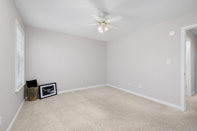 carpeted empty room featuring a ceiling fan and baseboards