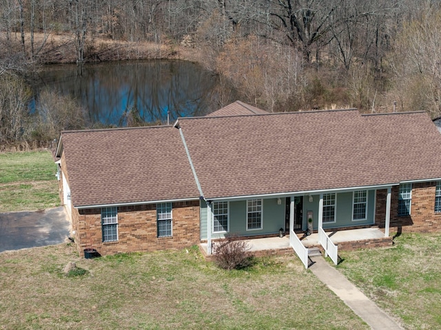 ranch-style home featuring brick siding, a shingled roof, a front yard, and a water view