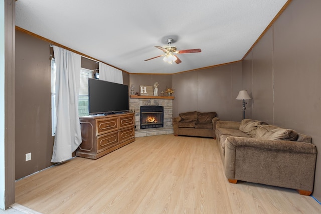 living area with light wood-style floors, a stone fireplace, ornamental molding, and a ceiling fan