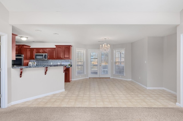 kitchen with dark brown cabinets, a chandelier, a kitchen bar, light carpet, and stainless steel appliances