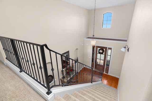 stairs with a wealth of natural light, baseboards, a towering ceiling, and wood finished floors