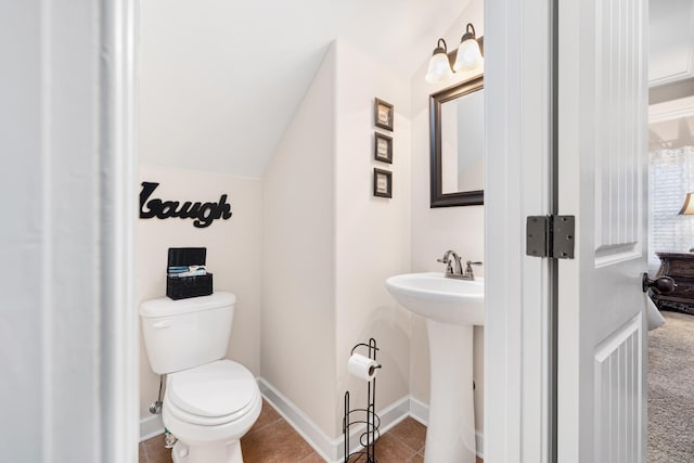 bathroom with tile patterned floors, toilet, lofted ceiling, a sink, and baseboards