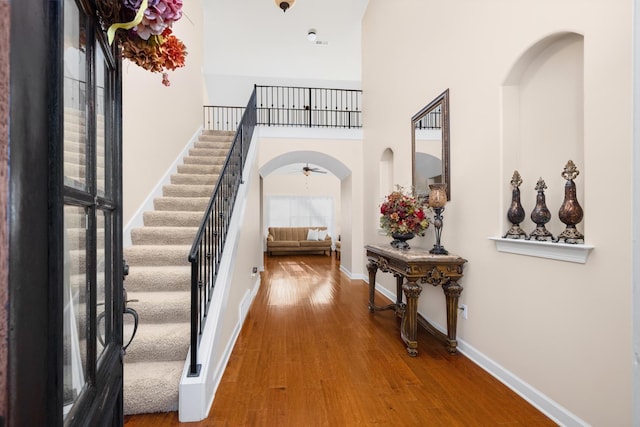 foyer entrance with wood finished floors, arched walkways, a high ceiling, baseboards, and stairs