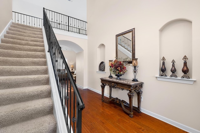 stairway with arched walkways, a high ceiling, baseboards, and wood finished floors