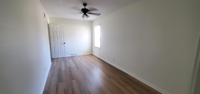 empty room with dark wood finished floors, visible vents, ceiling fan, and baseboards