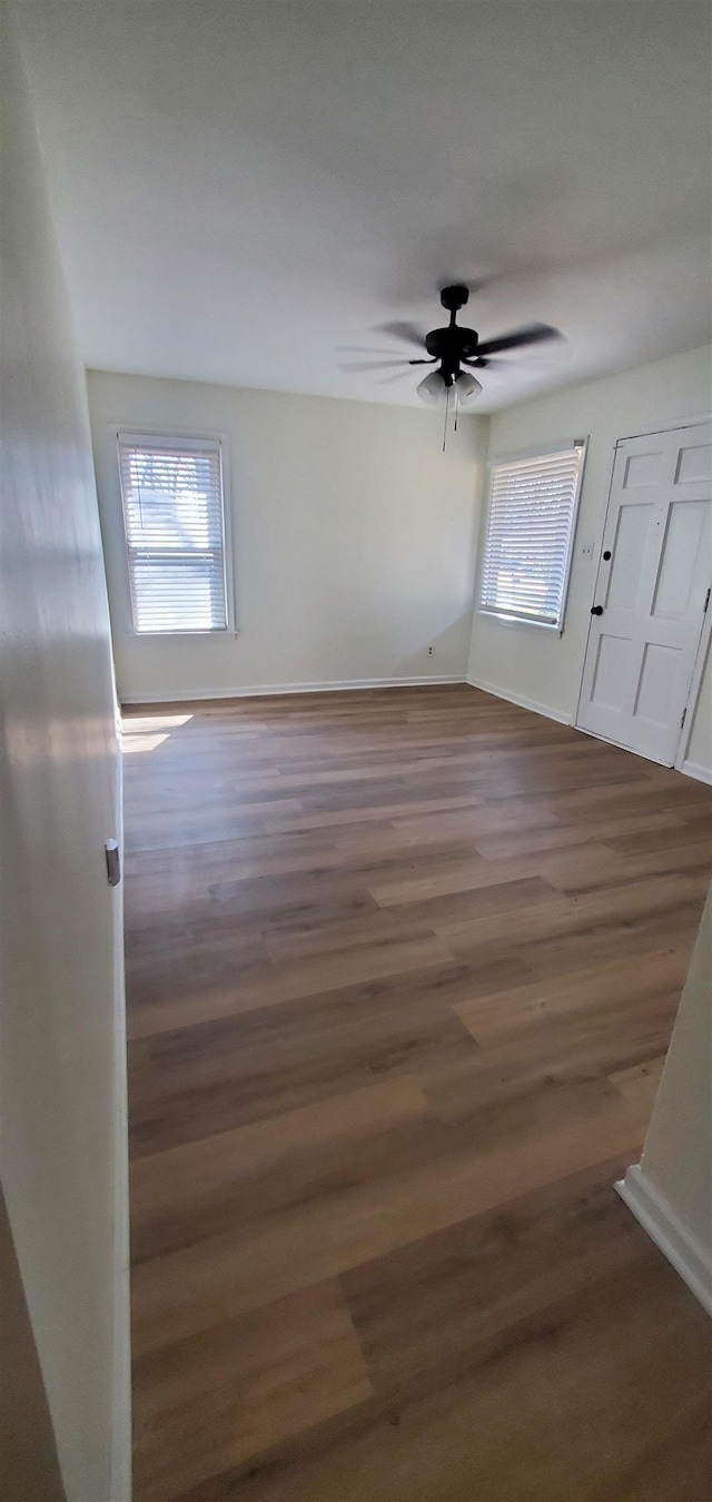 unfurnished room with baseboards, ceiling fan, and dark wood-style flooring