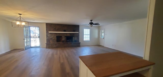 unfurnished living room with plenty of natural light, wood finished floors, a fireplace, and ceiling fan with notable chandelier