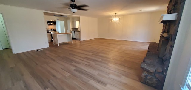 unfurnished living room with ceiling fan with notable chandelier, baseboards, and wood finished floors