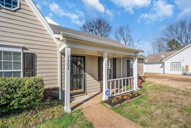 property entrance featuring a yard, covered porch, and roof with shingles