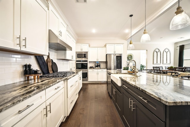 kitchen with a large island with sink, a sink, white cabinets, under cabinet range hood, and appliances with stainless steel finishes