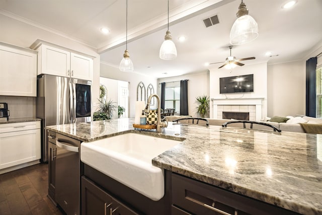 kitchen featuring a tile fireplace, decorative backsplash, a sink, appliances with stainless steel finishes, and crown molding