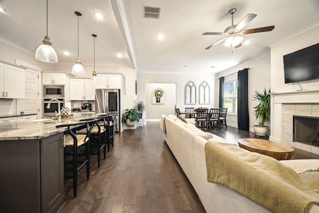 living room with dark wood finished floors, visible vents, crown molding, and baseboards