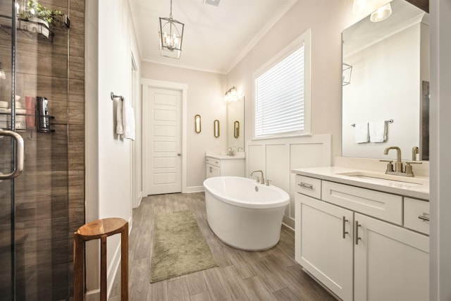 full bath featuring wood finished floors, a stall shower, a freestanding bath, ornamental molding, and a sink