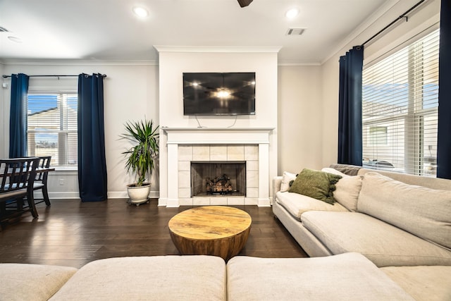 living area with a tile fireplace, crown molding, baseboards, and wood finished floors