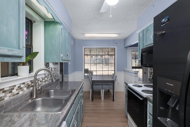 kitchen featuring a sink, electric range oven, black microwave, wainscoting, and refrigerator with ice dispenser