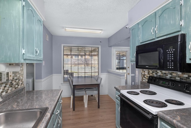 kitchen featuring a wainscoted wall, light wood finished floors, a sink, range with electric cooktop, and black microwave