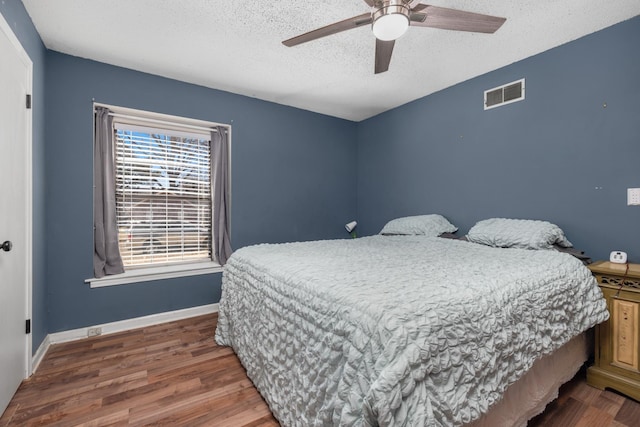 bedroom featuring visible vents, a ceiling fan, a textured ceiling, wood finished floors, and baseboards