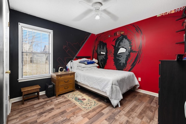 bedroom featuring an accent wall, wood finished floors, baseboards, and ceiling fan