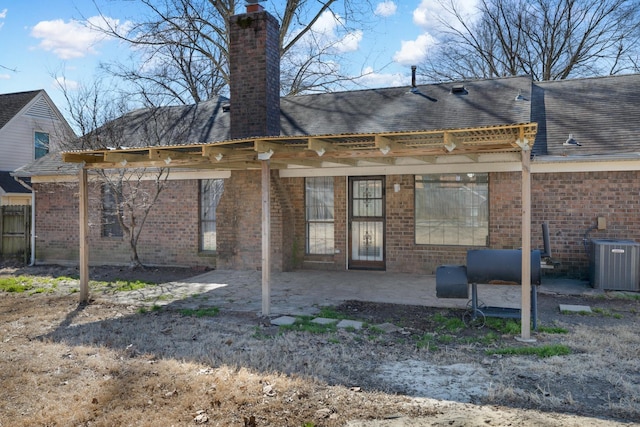 back of property featuring central AC unit, roof with shingles, a chimney, a patio area, and brick siding