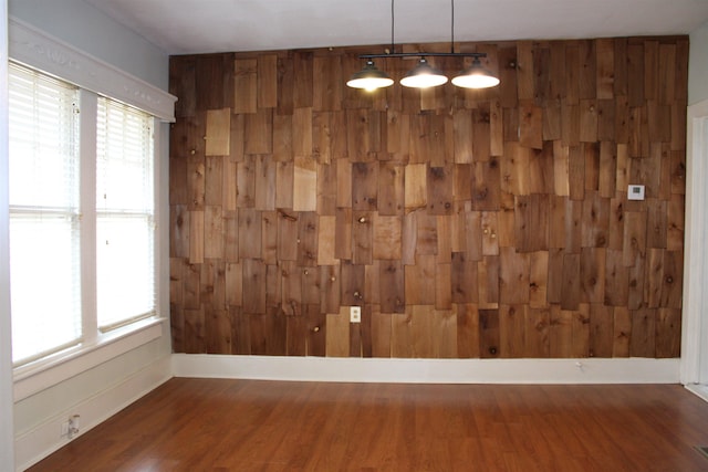 empty room with plenty of natural light, wooden walls, and wood finished floors