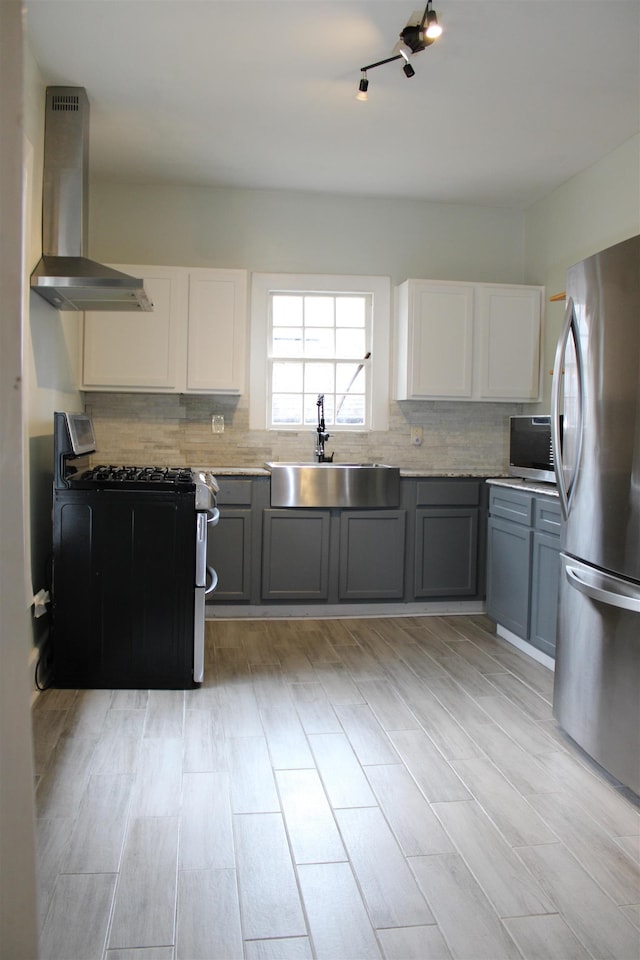 kitchen featuring a sink, stainless steel appliances, white cabinetry, wall chimney exhaust hood, and backsplash