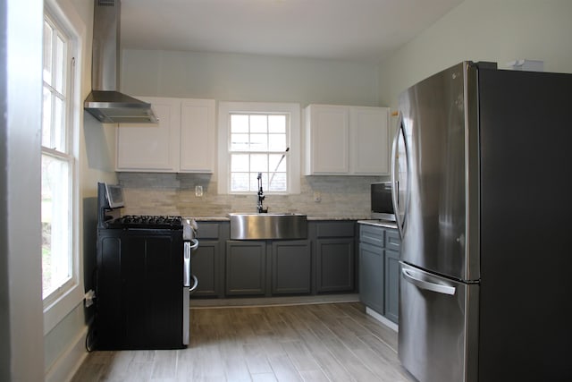 kitchen featuring backsplash, gas range oven, freestanding refrigerator, wall chimney exhaust hood, and a sink