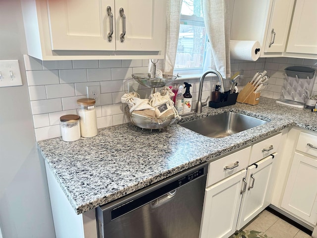 kitchen featuring light stone counters, a sink, white cabinets, and stainless steel dishwasher