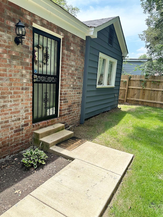 property entrance featuring a yard, fence, and brick siding