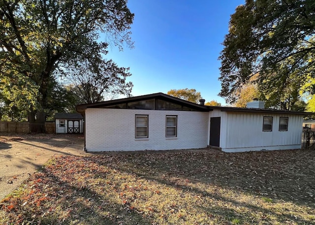 back of house with brick siding, fence, a chimney, an outdoor structure, and a storage unit