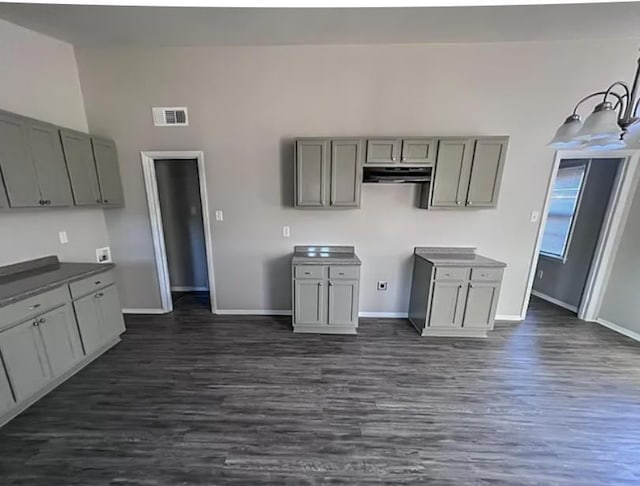 kitchen featuring baseboards, visible vents, dark wood-style flooring, gray cabinetry, and under cabinet range hood