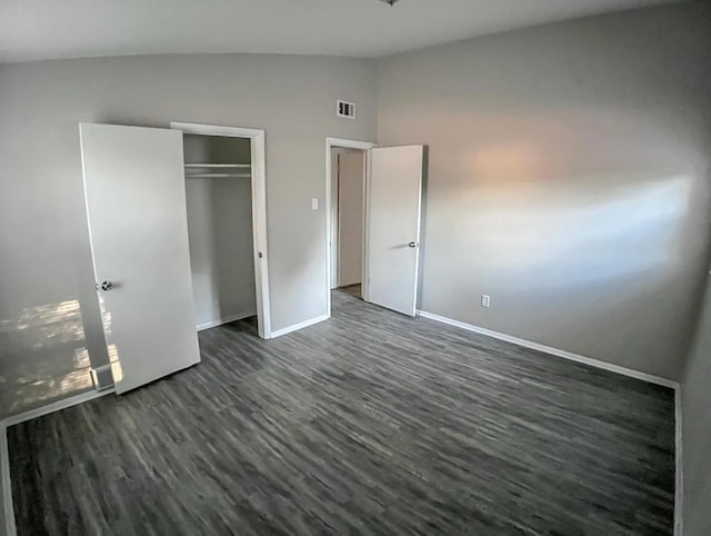 unfurnished bedroom with visible vents, dark wood-type flooring, baseboards, lofted ceiling, and a closet