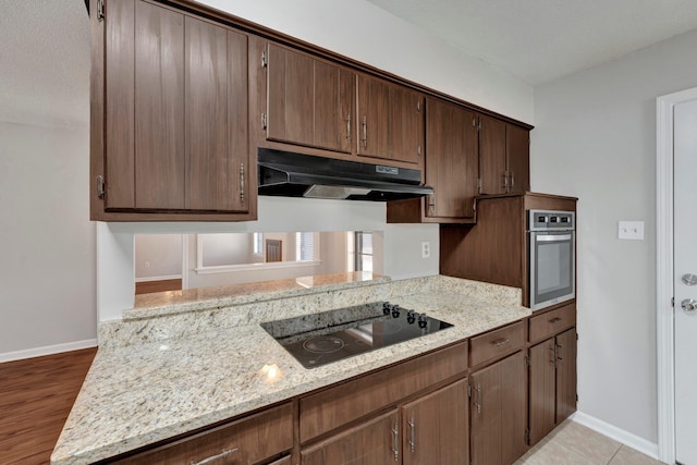 kitchen with stainless steel oven, black electric stovetop, baseboards, and under cabinet range hood